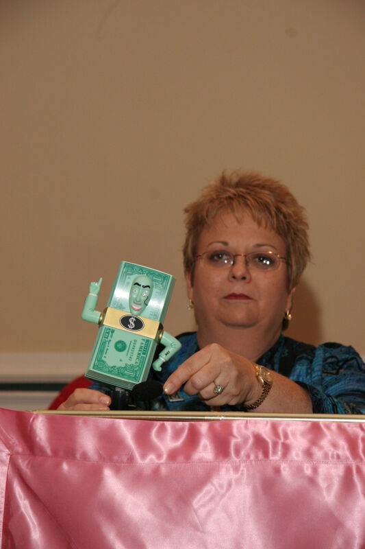 Kathy Williams With Dollar Bill Action Figure at Thursday Convention Session Photograph 1, July 13, 2006 (Image)