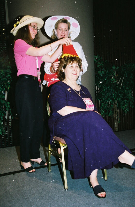 Unidentified Phi Mu Placing Hat on Mary Jane Johnson at Convention Officers' Luncheon Photograph 1, July 4-8, 2002 (Image)