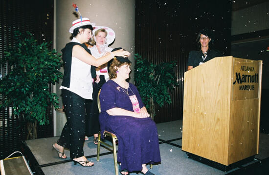 Unidentified Phi Mu Placing Hat on Mary Jane Johnson at Convention Officers' Luncheon Photograph 2, July 4-8, 2002 (image)