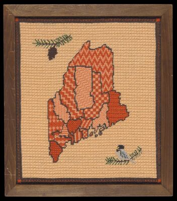 [Sampler of a map of Maine showing counties, Chickadee, pine cone; fabric in frame]