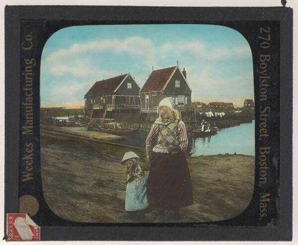 [Two girls standing infront of two houses on a shoreline]