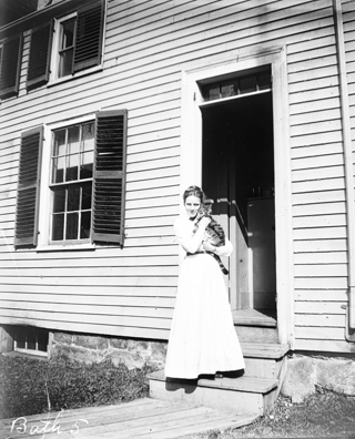 Frances standing on parsonage porch steps with cat, Ted.
