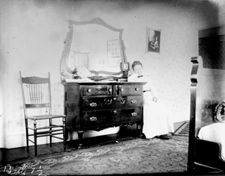 Bedroom showing corner of bed with Frances Yale sitting by bureau