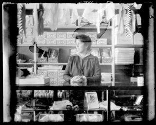 Woman clerk at counter of millinery shop