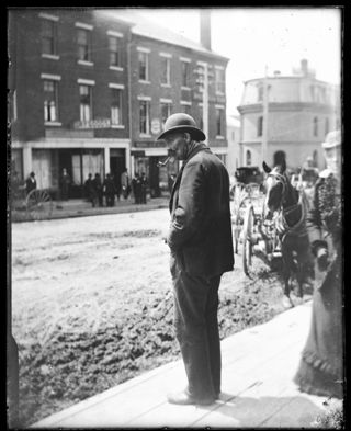 Little Lomard (?) Man smoking pipe and looking at Main Street with old Custom House in distance