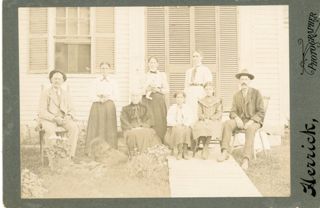 six women, two men, and dog sit outside house