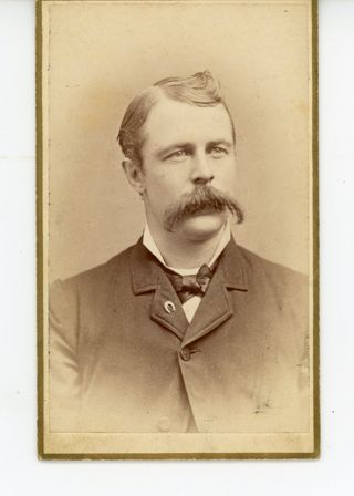 Man with dark hair dark suit and large mustache