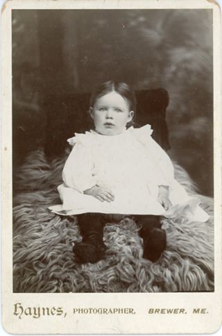 Portrait of dark haired baby in white dress and black stockings