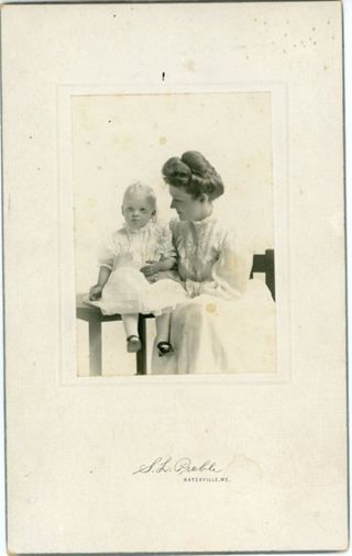 Baby wearing short white dress next to woman in white dress