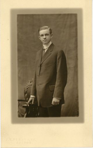 Man standing in dark suit next to a chair