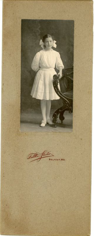 Young girl in white dress posed next to chair