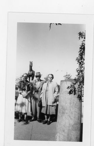 B&W photo of 2 women and 1 man standing in front of a statue of a horse