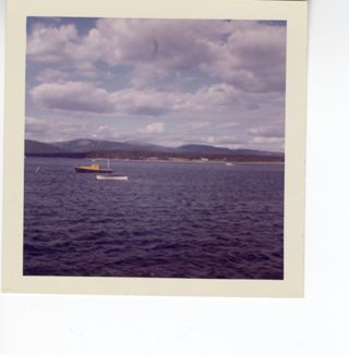Color photograph of two boats with ocean and mountains in the background