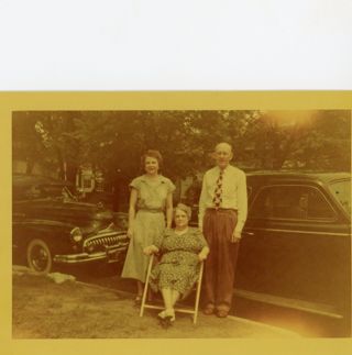 Yellowed color photograph of 3 people posed outside next to a car, 1949