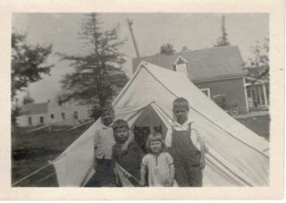 Four children outside their tent near old red store